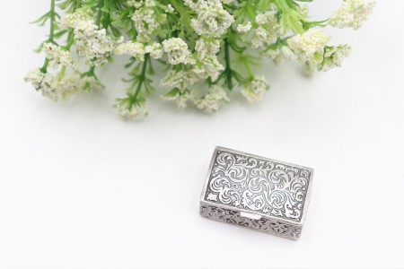 Caixa de comprimidos rectangular em prata com relevos na tampa e envolvência